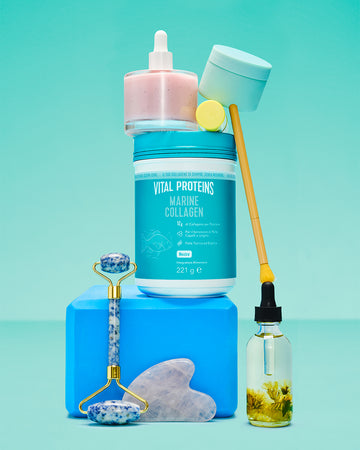 Vital Proteins Marine Collagen container surrounded by skincare items including a jade roller, facial oil, serum bottle, and beauty tools on a blue background.