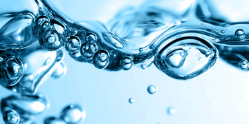 A close-up of crystal-clear water with bubbles and ripples, captured in motion. The blue tones emphasize the freshness and fluidity of the liquid.