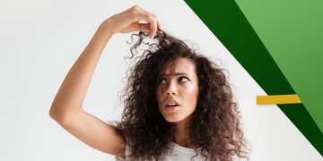 A young woman with voluminous curly hair looking frustrated as she examines a section of her hair. She wears a white t-shirt against a white background with abstract green and yellow geometric shapes.