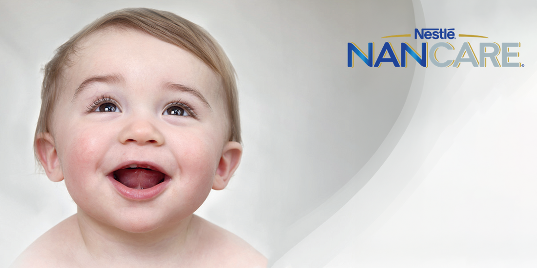 A promotional advertisement for Nestlé NANCARE featuring a close-up of a happy baby with bright eyes and an open-mouthed smile. The baby has fair skin and short brown hair. The background is soft and white with a gradient effect, giving a clean and gentle aesthetic. The Nestlé NANCARE logo is positioned in the top right corner in blue and gold text, emphasizing the brand’s baby nutrition and care products.